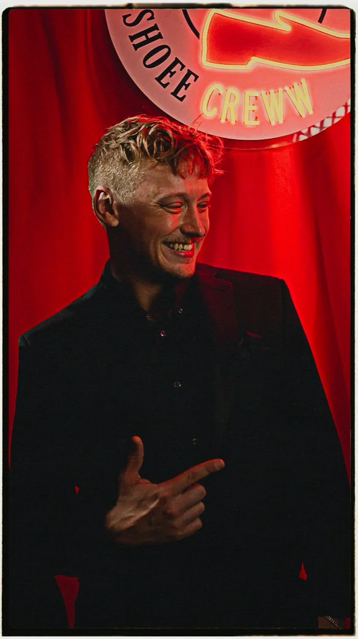 Portrait of Easton Thomas in a dark jacket in front of a red curtain